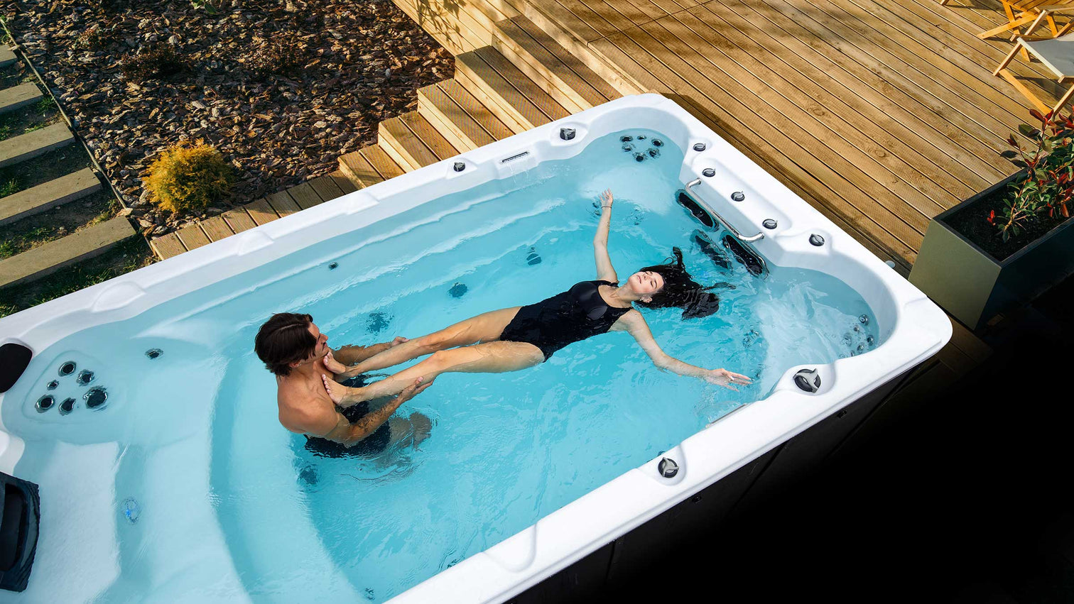 Two people swimming and floating in a Northern Leisure swim spa on a cedar deck