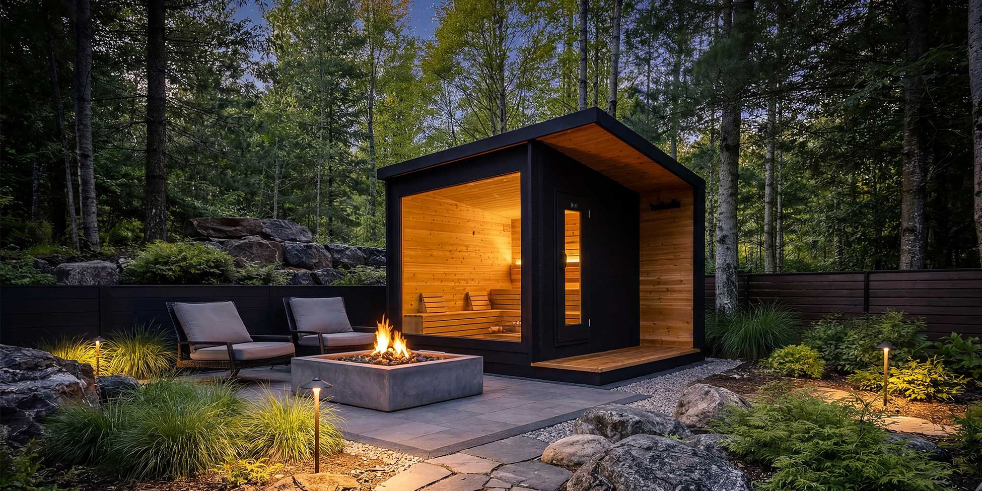 A lit modern cedar sauna beside a fire pit on a wooded Canadian property at dusk